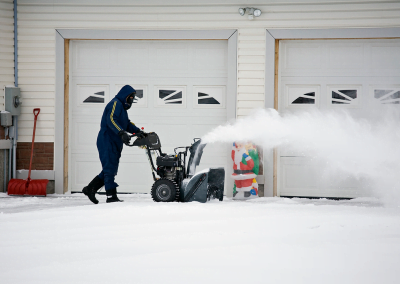 A man using a snow blower to remove snow from driveway