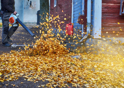A man using a leaf blower to remove leaves in backyard